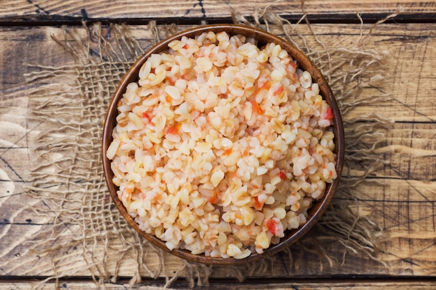 Boiled bulgur with tomatoes in a wooden bowl.