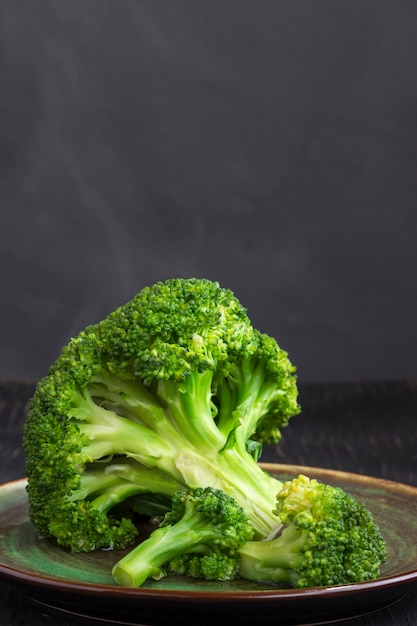 Boiled cabbage broccoli in a plate on black. Steam on cabbage