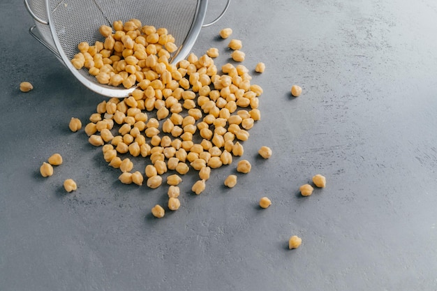 Boiled chickpeas spill out from sieve Garbanzo grains Eco product Dry peas Copy space Nut seeds Organic food Vegan ingredient