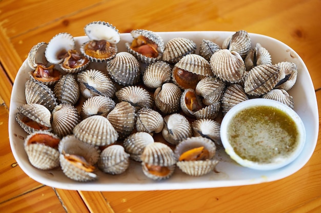 Vongole bollite e salsa di pesce piccante e acida servita su un piatto bianco e posta su un tavolo di legno frutti di mare popolari in thailandia cibo locale