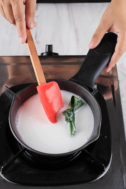 Foto latte di cocco bollito in padella di ferro con foglie di pandan per il dessert indonesiano thailandese vietnamita