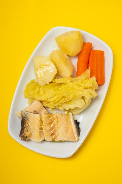 Boiled cod fish with boiled vegetables on white dish