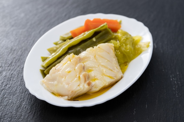 Boiled cod fish with vegetables on white dish