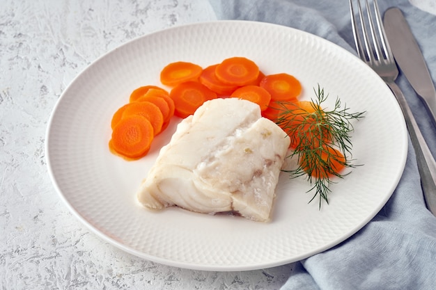 Boiled codfish with carrot and dill on white plate