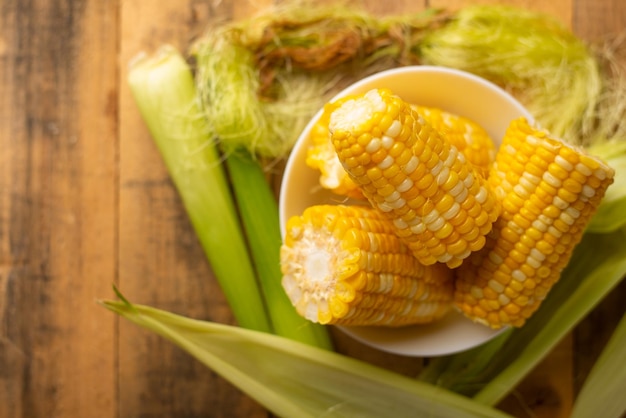 Boiled corn cob in a plate with butter on wooden textures and green stalks of corn tasty homemade food for a picnic with space