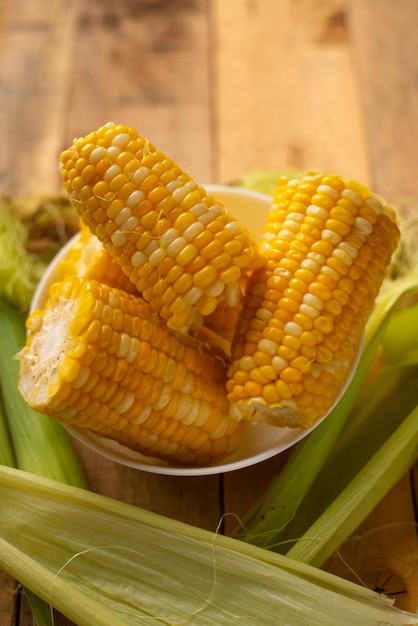 Boiled corn cob in a plate with butter on wooden textures and green stalks of corn tasty homemade food for a picnic