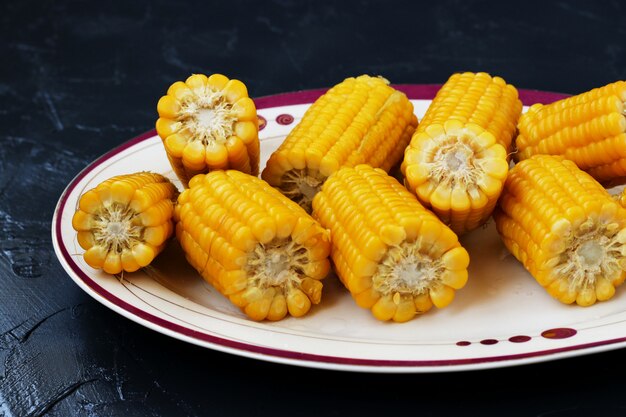 Photo boiled corn is located on a plate on a dark background