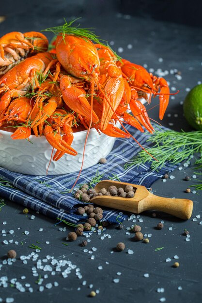 Foto i gamberi bolliti giacciono in un piatto profondo rotondo, erbe fresche, su uno sfondo nero, con lime e limone