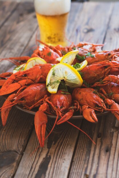 Boiled crayfish served on a platter with herbs and lemon on wooden table