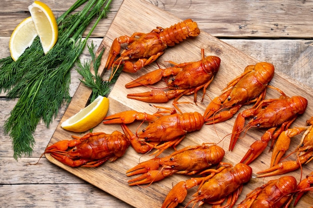 Boiled crayfish on a wooden aged table and a wooden board with dill and lemon.