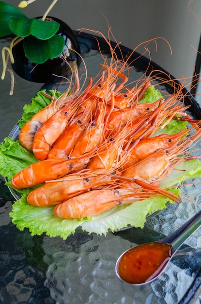 Boiled delicious king shrimp on green lettuce leaves with Thai sweet and sour sauce on a glass table