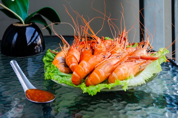 Boiled delicious king shrimps on green lettuce leaves with Thai sweet and sour sauce on glass table