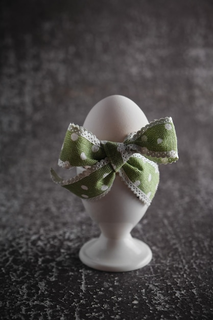 Photo boiled easter egg with green bow in holder on dark background