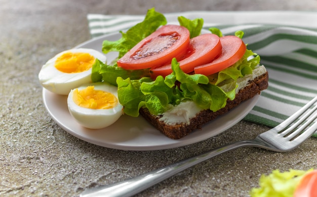 Boiled eggs cut in half and sandwich with rye bread, cream cheese, sliced tomatoes and fresh lettuce for healthy breakfast/lunch.