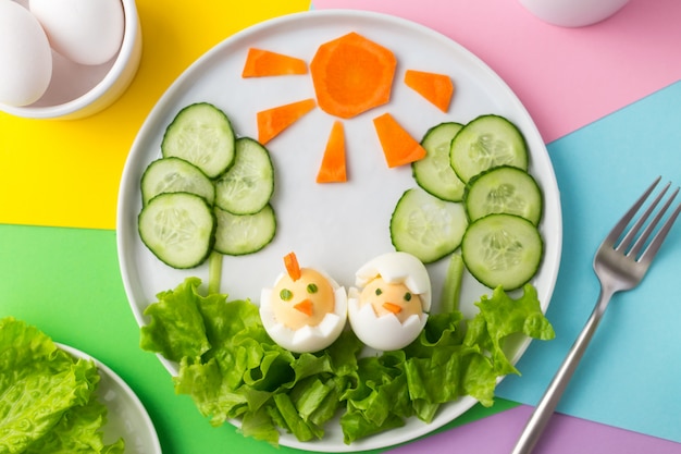 Photo boiled eggs decorated like chickens, carrot sun and cucumber tree