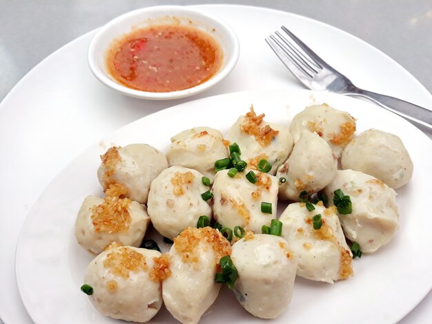 Photo boiled fish balls in a white plate with a small bowl of spicy fish ball sauce