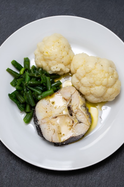 Boiled fish with boiled vegetables on white plate