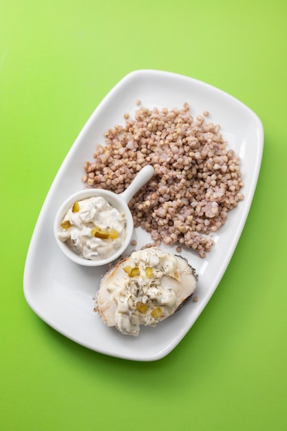 Boiled fish with buckwheat and sauce on white dish on green table