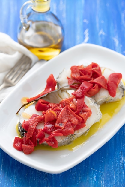 Boiled fish with red pepper and olive oil on white dish