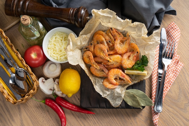 Boiled king prawns with lemon in baking paper on a wooden chopping board