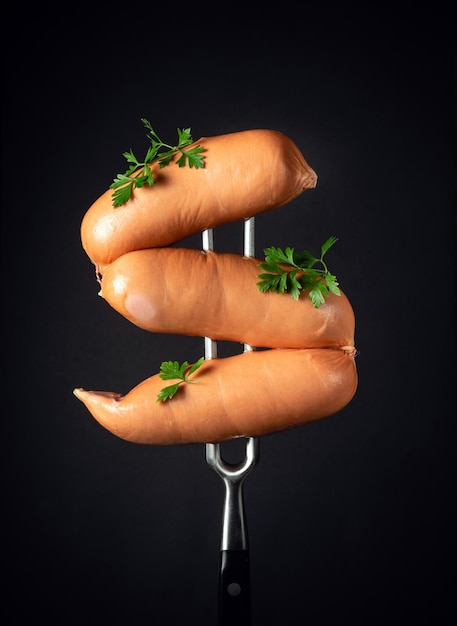 Boiled milk sausages or frankfurters with parsley on a fork on a black background Street food concept
