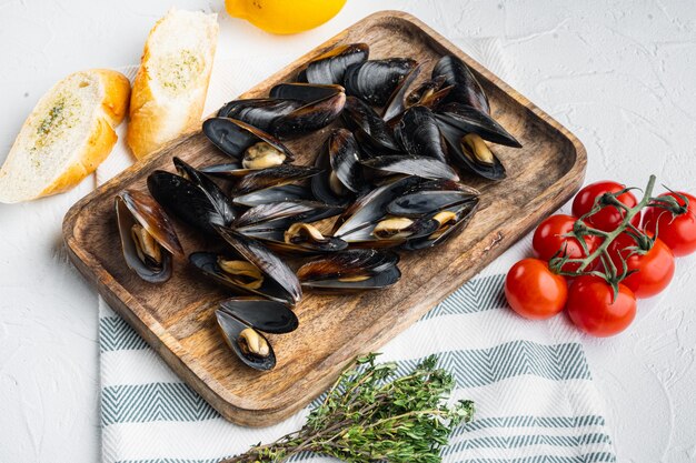 Boiled mussels in garlic sauce with parsley and ingredients, on wooden tray, on white table