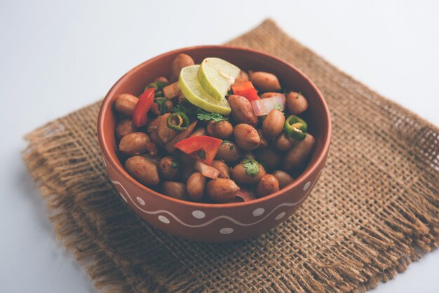 Boiled Peanut Chaat or Chatpata sing dana or shengdana or mungfali. served in a ceramic bowl over moody background