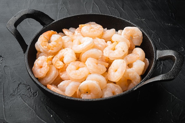 Photo boiled peeled prawns set, in frying cast iron pan or pot, on black stone table