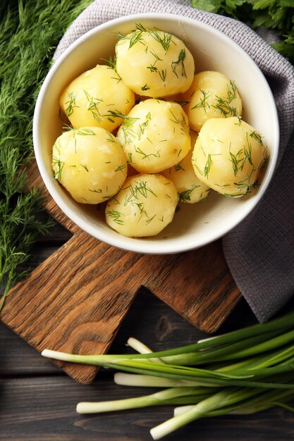 Boiled potatoes with greens in bowl on table close up