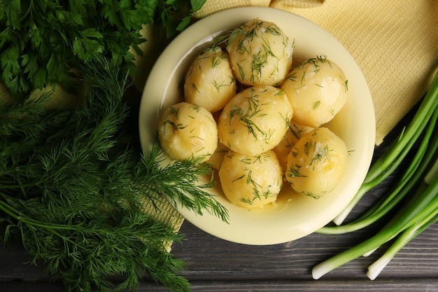 Boiled potatoes with greens in bowl on table close up