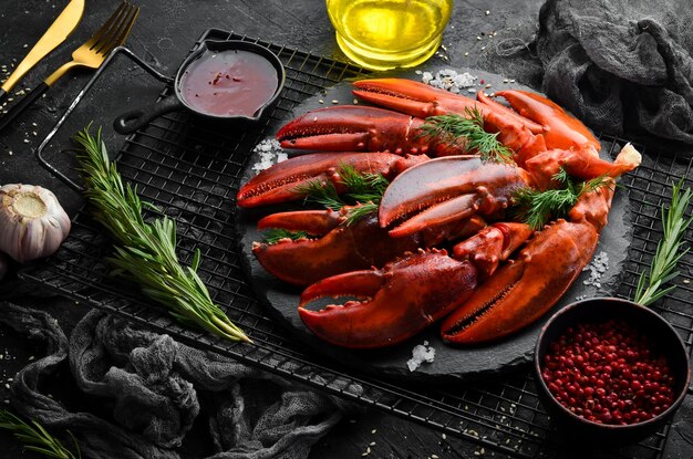 Boiled red lobster claws with spices and parsley on a black\
stone plate on a black background rustic style seafood\
delicacies