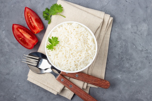 Boiled rice and cutlery in a bowl. Gray stone background. Top view.