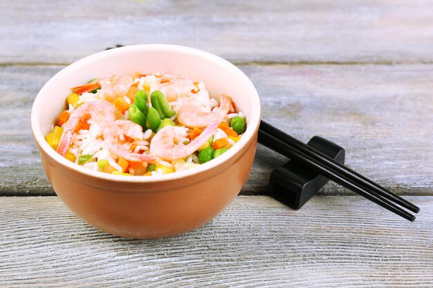 Вареный рис с креветками и овощами на деревянном фоне