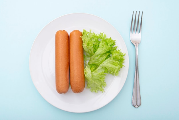 Boiled sausages on white ceramic plate with green, morning breakfast, top view, lay out