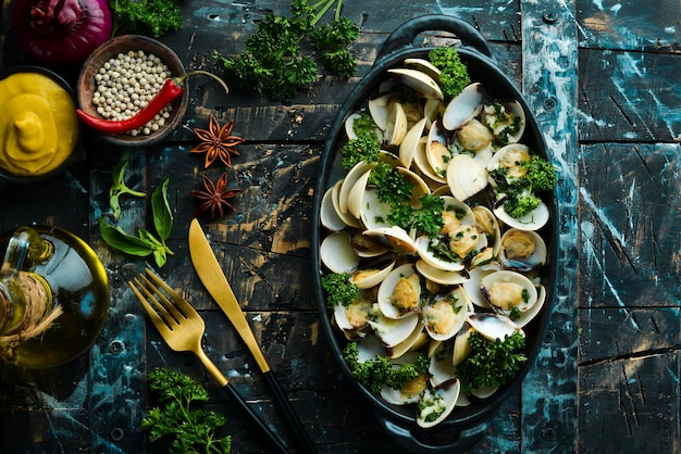 Boiled shellfish in shells with garlic and parsley in a black plate Seafood Top view Free space for text