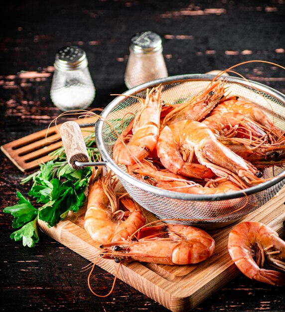 Boiled shrimp in a colander on a cutting board with parsley