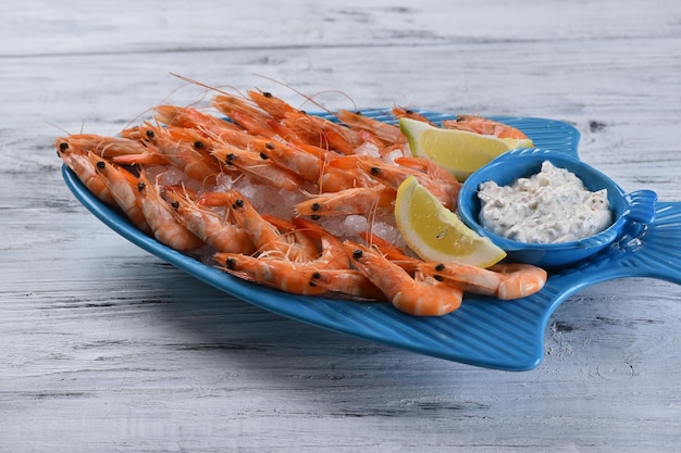 Boiled shrimp with garlic sauce and lemon, on an ice pillow in a blue fish-shaped plate, seafood