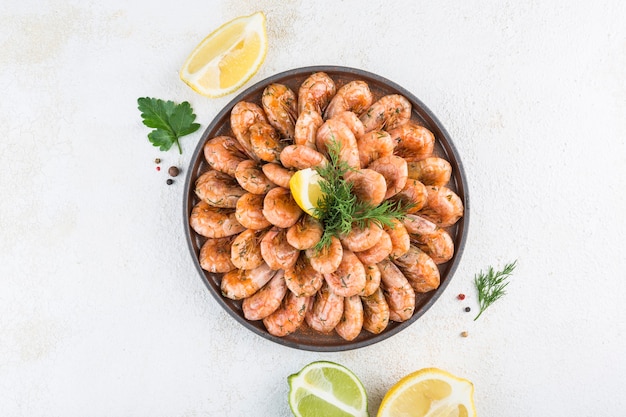 Photo boiled shrimp with lemon slices on a dark plate on a light background. top view with a copy space for the text. seafood appetizer with beer. horizontal orientation.