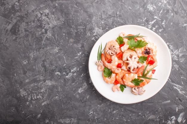 Boiled shrimps or prawns and small octopuses with herbs on white ceramic plate on a black concrete background. Top view.