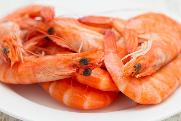 Boiled shrimps on white dish on wooden surface