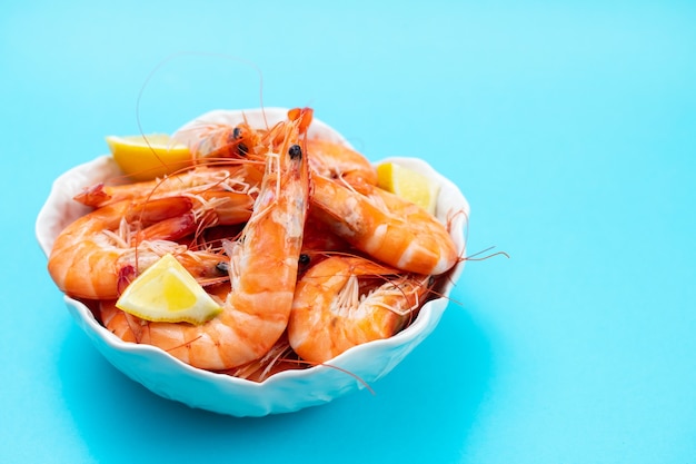 Gamberi bolliti con limone fresco in una ciotola bianca sul tavolo blu