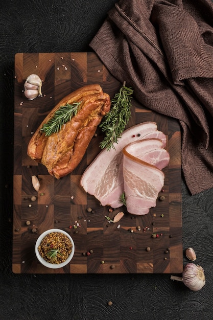 Boiled smoked pork brisket on a wooden board with grainy mustard and fresh herbs on a dark background. Top view. Vertical orientation with a copy space for the text.