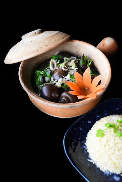 黒の背景の側面図に野菜と鍋に豚肉を詰めたゆでたカタツムリ