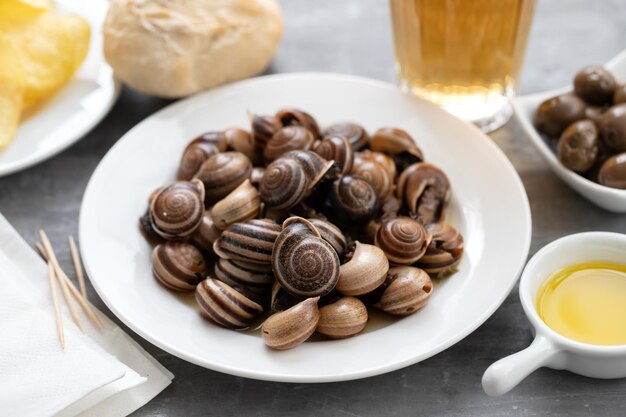 Boiled snails with bear bread olives and potato chips on ceramic