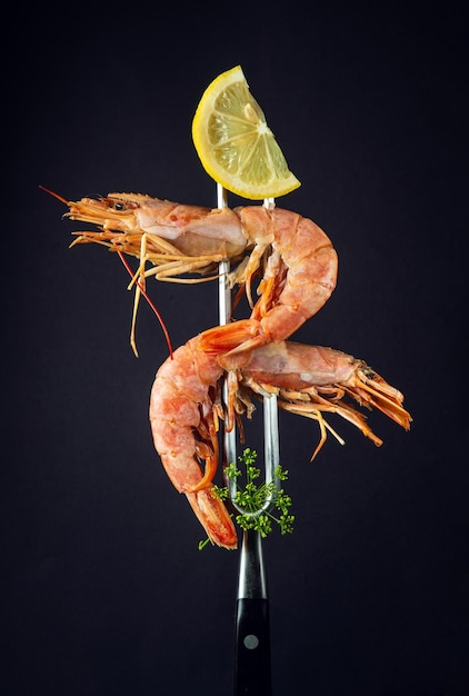 Boiled tiger prawns or king shrimps with parsley and a slice of
lemon on a fork delicious street food idea on black background