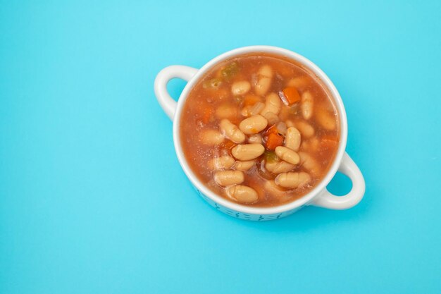 Boiled white beans with vegetables and sauce on white bowl