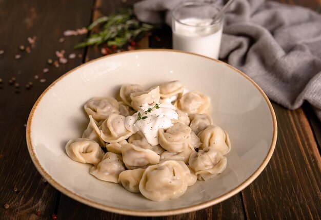 boiled white dough dumplings with meat butter pepper and sour cream sauce in a plate on a wooden t