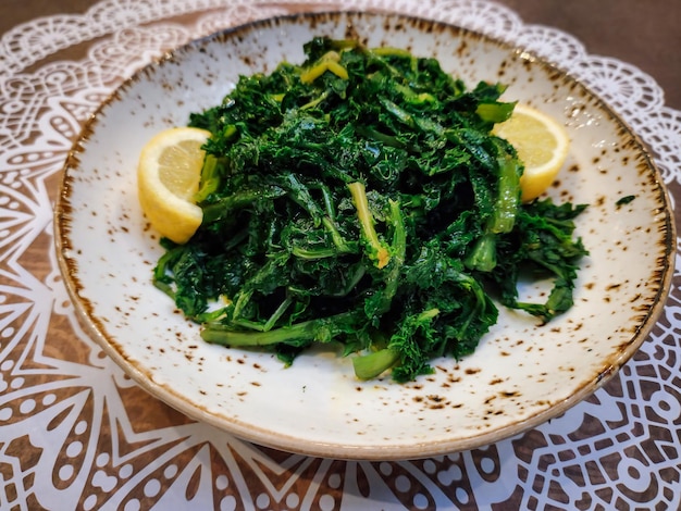 Boiled wild cooked greens close up top view served with lemon and olive oil on a dish