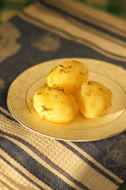 Boiled young potatoes with dill on a white plate Vegetarian food concept Closeup of potatoes on a blue napkin