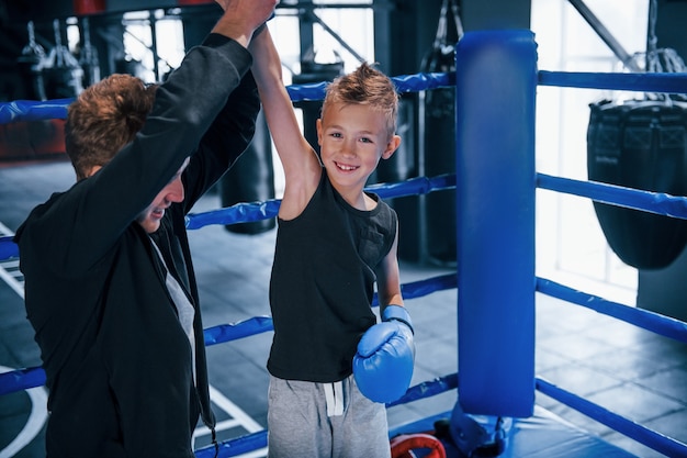 Bokscoach die met jongen in de ring staat en samen de overwinning viert.